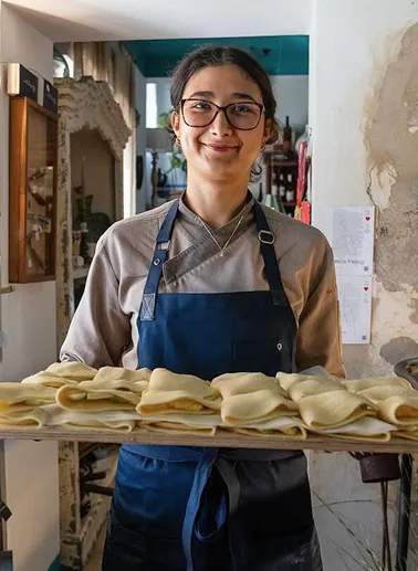 Anna, una cuoca del ristorante, con in mano un vassoio di pasta fresca ripiena appena preparato nel ristorante da Alcide a Venturina, in Toscana.