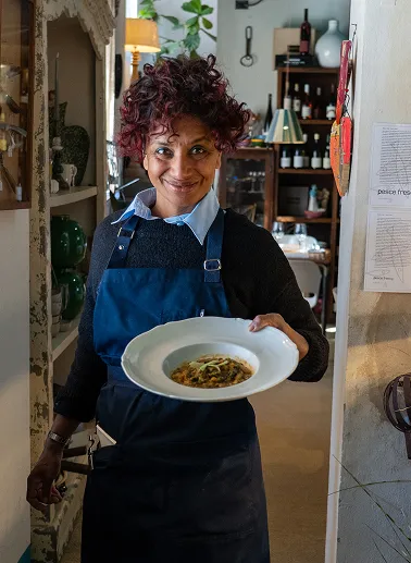 Carmen, una cuoca della brigata del ristornate in Toscana, con in mano un piatto con minestra di pesce appena preparato nel ristorante da Alcide a Venturina, in Toscana.