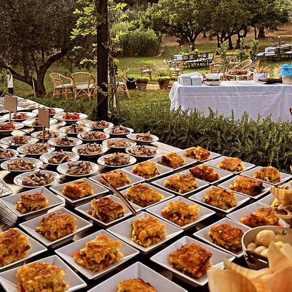 Catering allestito e preparato dal team da Alcide, in un grande giardino in Toscana una tavolata piena di mono porzioni di piatti tipici del ristorante.