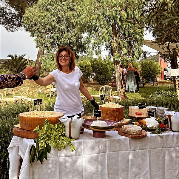 Catering allestito e preparato dal team da Alcide, Francesca dietro il tavolo dei formaggi del luogo porge un assaggio ad un cliente.