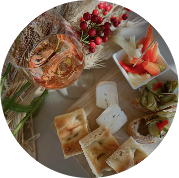 Servizio aperitivi presentato con una fotografia dall'alto di un tavolo allestito con cibo del luogo e vino rosato, curato dal team del ristorante da Alcide a Venturina, in Toscana.