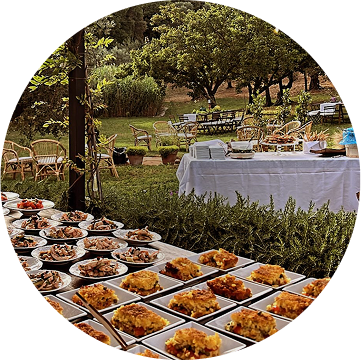 Servizio di catering presentato con una foto di un allestimento di tavoli con cibo e arredamento in un giardino in Toscana, curato dal team del ristorante da Alcide a Venturina, in Toscana.
